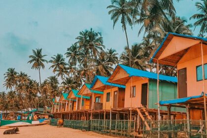 An image of blue and brown wooden houses near palm trees under blue sky during daytime in Goa.