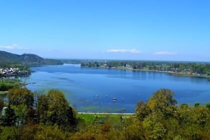 A picture of Manasbal Lake, the serene waters reflecting the surrounding lush green hills.