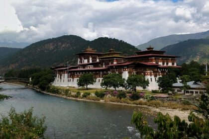 A scenic view of the palace at Punakha Region, surrounded by green mountains and calm water, one of the best places to visit in Bhutan in August.