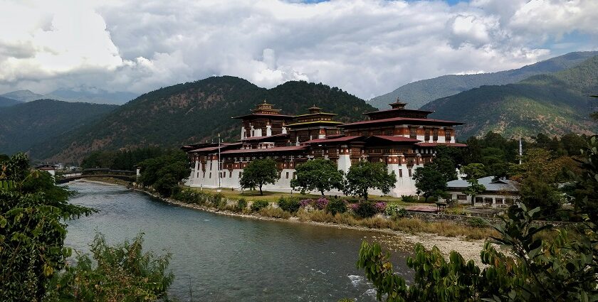 A scenic view of the palace at Punakha Region, surrounded by green mountains and calm water, one of the best places to visit in Bhutan in August.