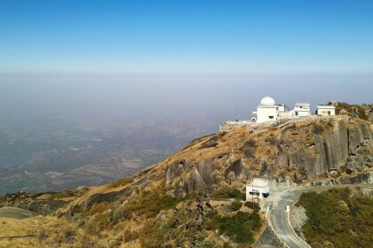 Top of the Mount Abu with white architectural buildings, rocky cliffs and a road passing.