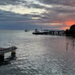Placencia in Belize with a calm water body, distant boats, small buildings and vibrant sky