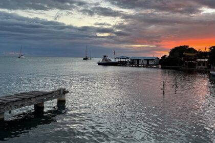 Placencia in Belize with a calm water body, distant boats, small buildings and vibrant sky