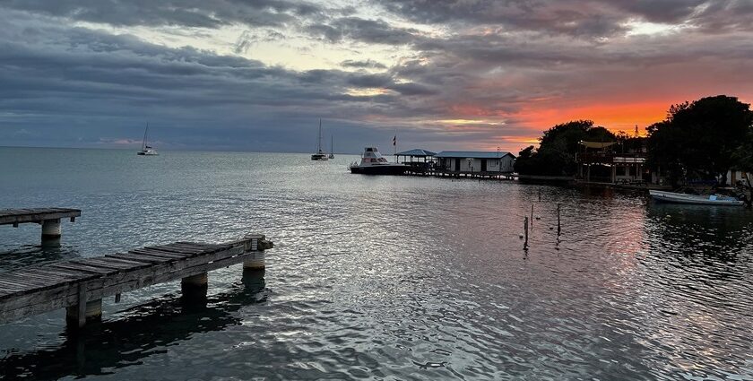Placencia in Belize with a calm water body, distant boats, small buildings and vibrant sky