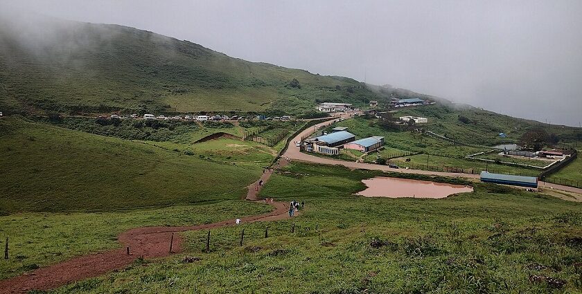 Foggy hillside view with scattered buildings, winding road, and lush green surroundings.