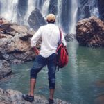 A man wearing a cap stands and marvels at the views of Sathodi Falls, one of the best places to visit near Dandeli.