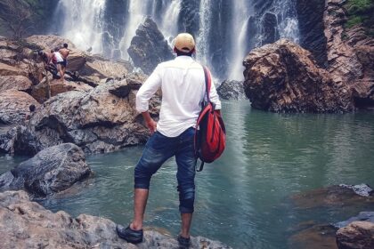 A man wearing a cap stands and marvels at the views of Sathodi Falls, one of the best places to visit near Dandeli.