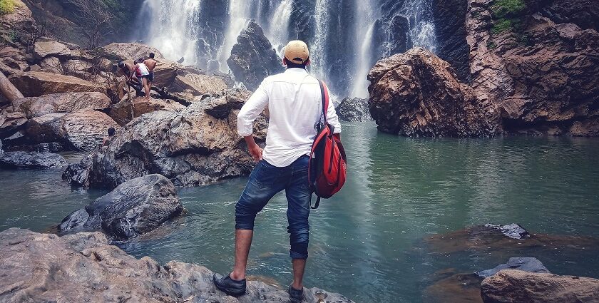 A man wearing a cap stands and marvels at the views of Sathodi Falls, one of the best places to visit near Dandeli.