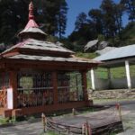 Small wooden temple with intricate carvings set amid lush green hills and pine trees Viewers of this file can see comments and suggestions