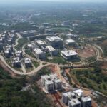 Modern campus buildings nestled among lush green hills under a cloudy blue sky view.