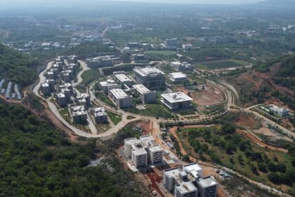 Modern campus buildings nestled among lush green hills under a cloudy blue sky view.