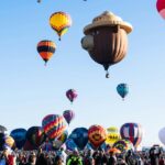 Several hot air balloons rising during Albuquerque International Balloon Fiesta with crowds watching the launch.