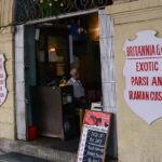Front of Café du Commerce in Belley with black awning, wooden barrels, and seating, one of the best cafes in Kalimpong.