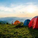 Two tents on a grassy hilltop under cloudy skies, perfect for camping in Karnataka.