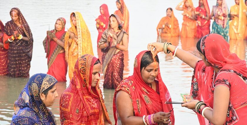 Women in traditional attire offering prayers during Chhath Puja at a riverbank.