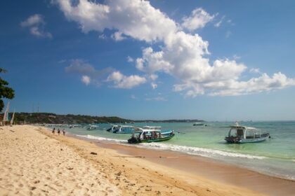 Sandy shore and calm waters with boats docked at Nusa Lembongan, one of the best islands in Bali.