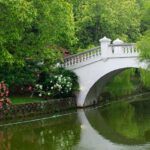 A white bridge over a calm water body surrounded by flowers and greenery, one of the scenic parks in Malaysia.