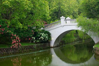 A white bridge over a calm water body surrounded by flowers and greenery, one of the scenic parks in Malaysia.