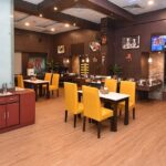 Interior of a modern restaurant in Siliguri with yellow chairs, wood flooring, buffet area