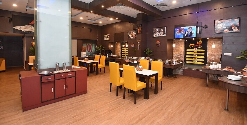 Interior of a modern restaurant in Siliguri with yellow chairs, wood flooring, buffet area