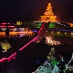 A night view of a park with an illuminated statue in Sikkim with a fountain in front.