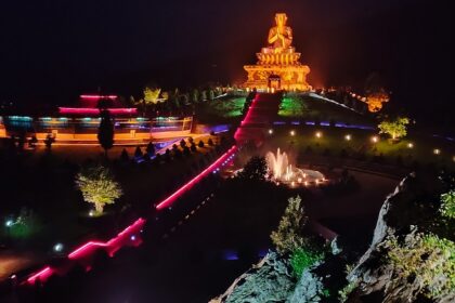 A night view of a park with an illuminated statue in Sikkim with a fountain in front.