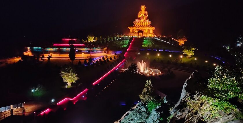 A night view of a park with an illuminated statue in Sikkim with a fountain in front.