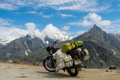 A winding dirt road passes through a vibrant green valley with scattered trees and peaks.