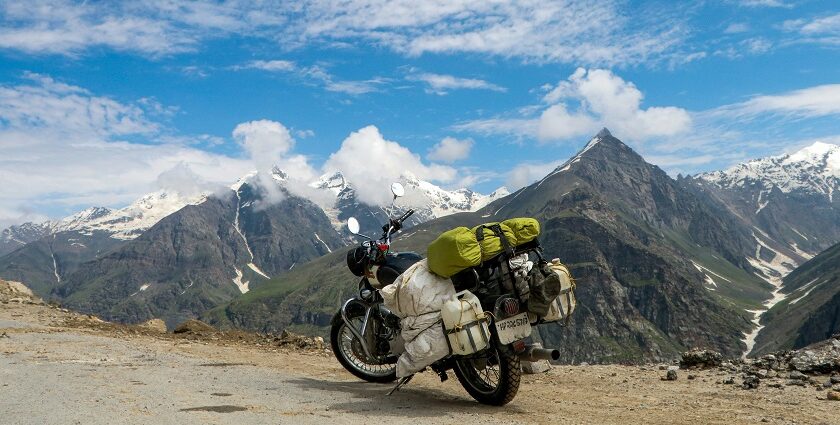 A winding dirt road passes through a vibrant green valley with scattered trees and peaks.