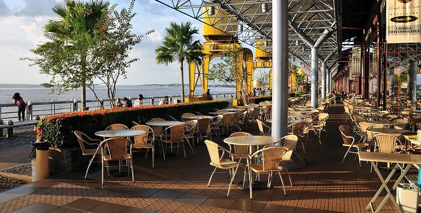 A waterfront outdoor cafe with many empty tables and chairs under a large, modern roof, one of the vegetarian restaurants in Singapore Little India.