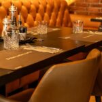 Warmly lit restaurant table with leather seating, glassware, and condiments neatly arranged, one of the restaurants in Jorhat.