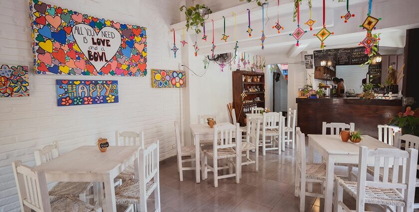 Bright restaurant with white wooden chairs, colourful wall art, hanging crafts and potted greens, one of the restaurants in Tezpur.