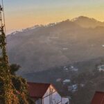 Snow-covered Kasauli hills are seen behind city buildings and telecom towers, showing snowfall in Kasauli.