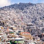 Scenic view of snowfall in Shimla with snow-covered roofs and mountain backdrop.
