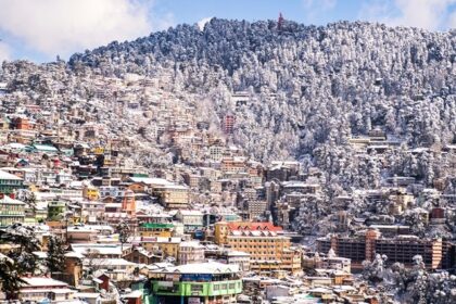 Scenic view of snowfall in Shimla with snow-covered roofs and mountain backdrop.