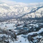 A person rowing a boat on Dal Lake against huge snow-covered mountains, showing snowfall in Srinagar.