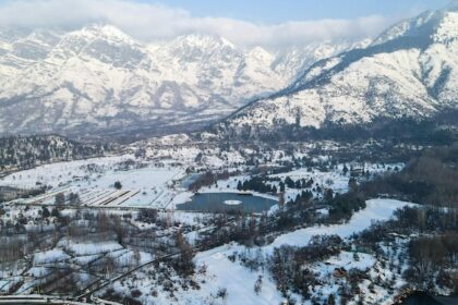 A person rowing a boat on Dal Lake against huge snow-covered mountains, showing snowfall in Srinagar.