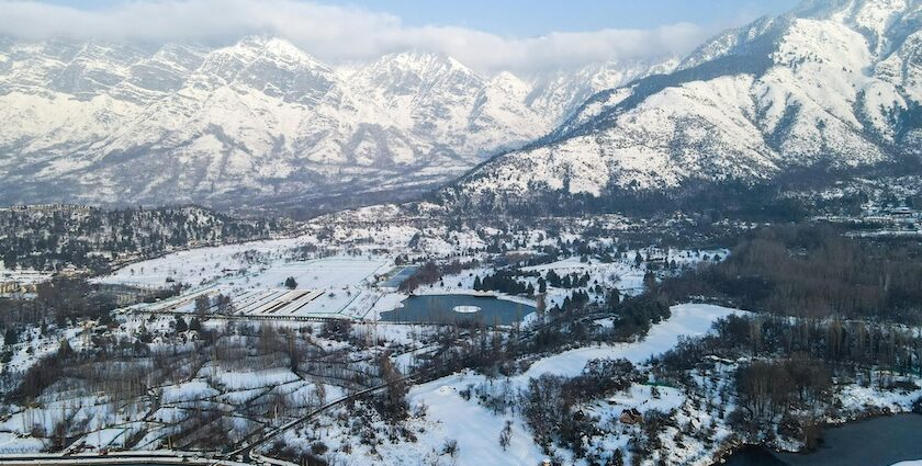 A person rowing a boat on Dal Lake against huge snow-covered mountains, showing snowfall in Srinagar.